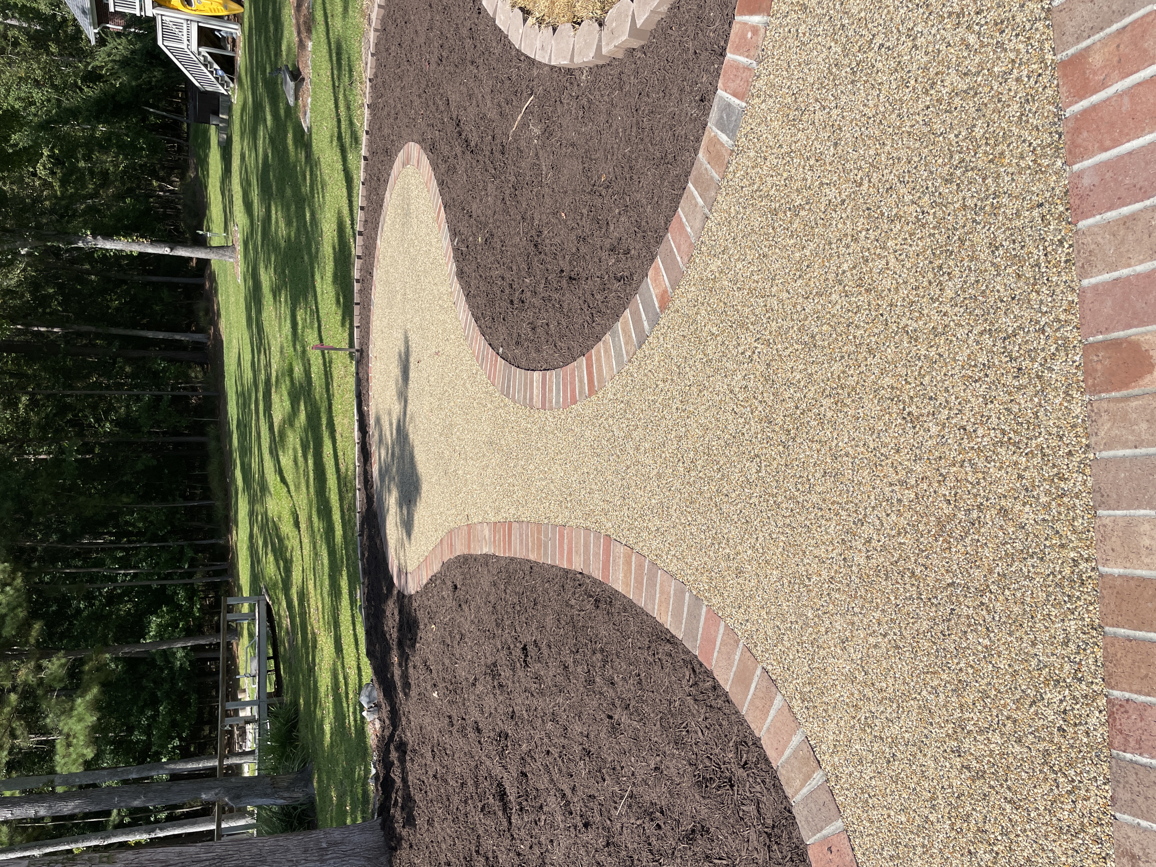 Winding brick-edged resin rock pathway through backyard garden