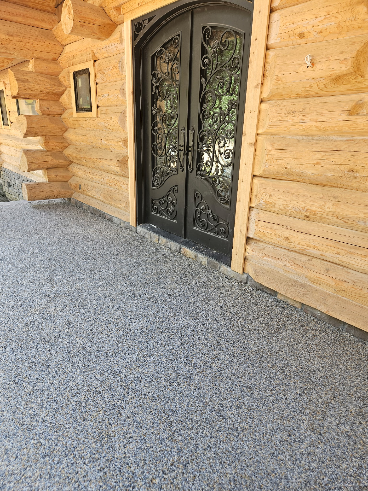 Resin bound stone porch at log cabin with ornate iron doors